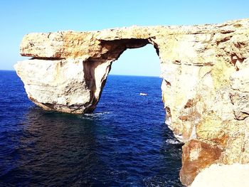 Rock formation in sea against clear blue sky