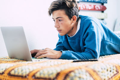 Teenager boy using laptop on bed at home