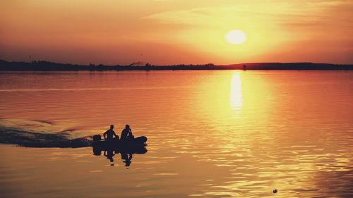 Silhouette people on lake against sky during sunset