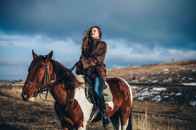 Woman riding horse on land against cloudy sky