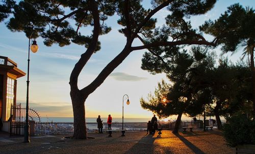 People on beach by street against sky during sunset