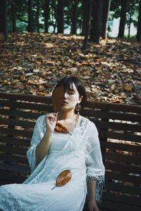 Young woman sitting on bench against trees