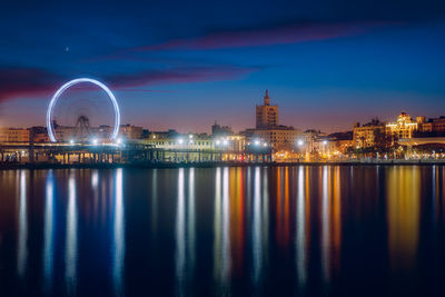 Illuminated city by river against sky at night