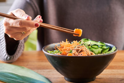 Close-up of hand holding salad in bowl on table