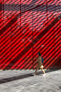 Person walking on footpath against red wall