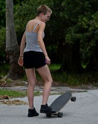 Rear view of woman with skateboard standing on road