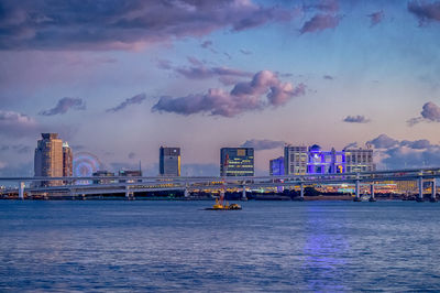 Sea by buildings against sky during sunset