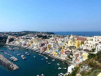 High angle view of townscape by sea against clear blue sky