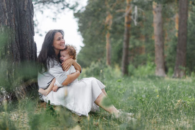 Young woman smiling while sitting on land in forest