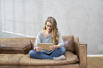 Blond woman sitting on leather couch using tablet