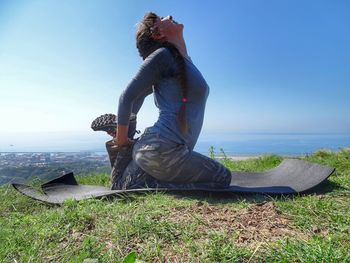 Side view of woman practicing yoga against sea and sky during sunny day