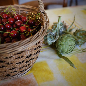 Close-up of cherries in basket by artichoke on table