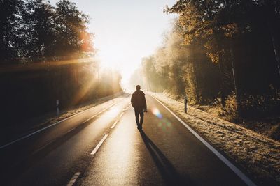 Rear view of man walking on road during sunrise