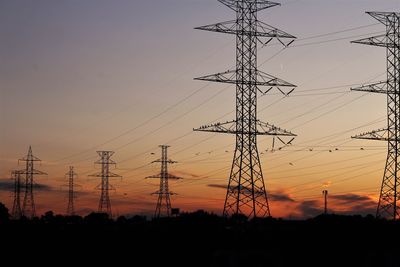 Low angle view of silhouette electricity pylon against sky during sunset