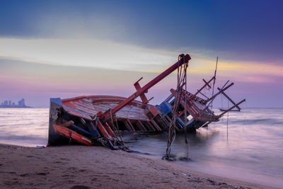 Fishing boat on beach against sky during sunset