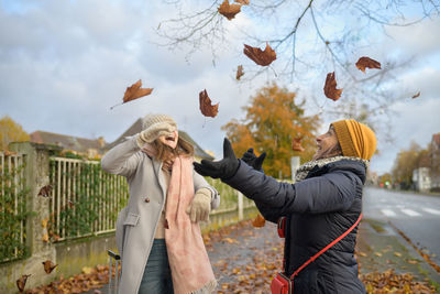 Couple of happy women playing with the leaves in the city in warm clothes