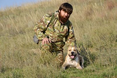 Man wearing camouflage clothing with dog on field