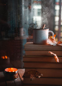 Stacked books and hot tea against rainy window