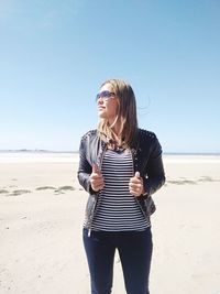 Mature woman wearing sunglasses standing on beach against clear sky during sunny day