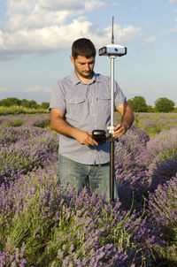 Surveyor with theodolite on lavender field against sky