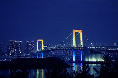 Illuminated rainbow bridge over bay in city at night