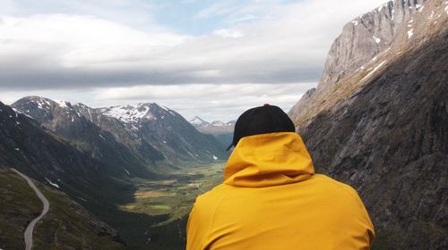 Rear view of man looking at mountains against cloudy sky