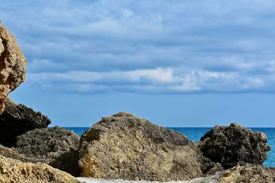 Rocks by sea against cloudy sky