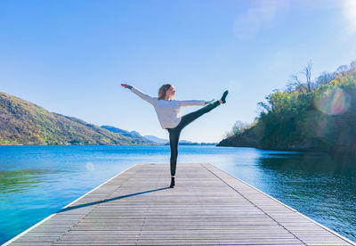 Woman exercising with arms outstretched on pier against lake