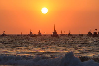 Silhouette sailboat sailing on sea against orange sky