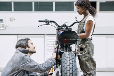 Diverse male and female mechanics in workwear fixing motorcycle together in bright garage