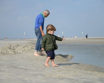 Grandfather with grandson enjoying at beach against sky during sunny day