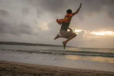 Man jumping at beach against sky