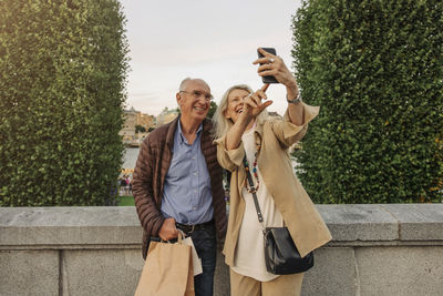 Happy senior woman taking selfie with man leaning on railing