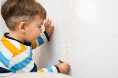 Cute boy drawing on wall at home