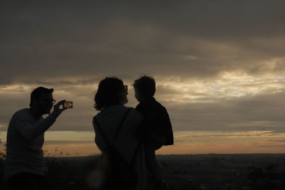 Man photographing mother with boy from mobile phone against sky