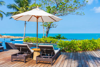 Lounge chairs by swimming pool at beach against sky