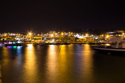 Illuminated city by sea against sky at night