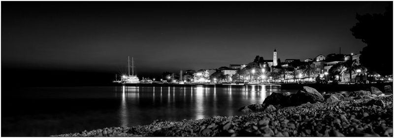 Illuminated buildings by sea against sky at night