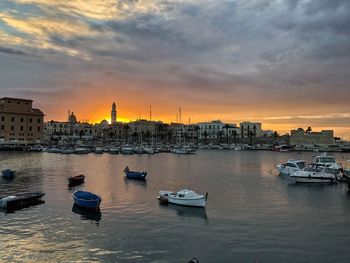 Sailboats moored in harbor against sky during sunset