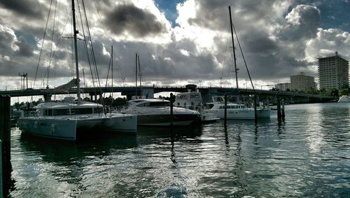 Boats in harbor against cloudy sky