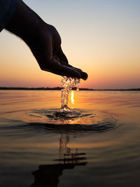 Person hand by sea against sky during sunset