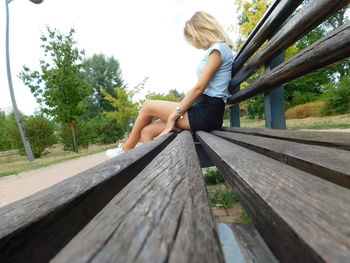 Woman sitting on wooden footbridge against sky
