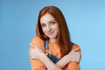 Woman hugging self against blue background