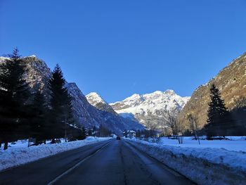 Road amidst snowcapped mountains against clear blue sky during winter