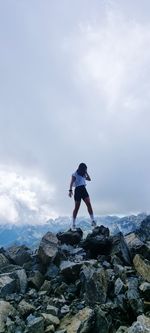 Rear view of woman standing on rock against sky