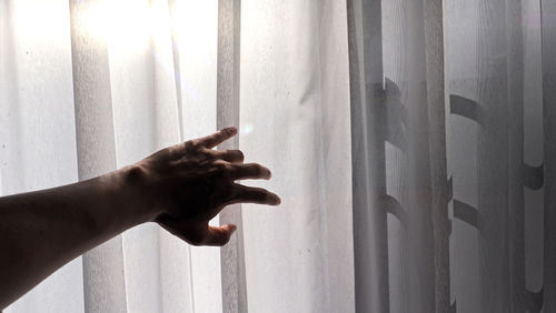 Close-up of hand touching window against curtain