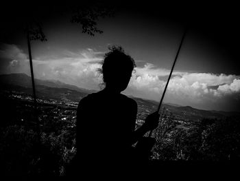 Rear view of silhouette man overlooking cityscape against sky
