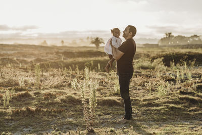 Father playing with young girl at beach during sunset