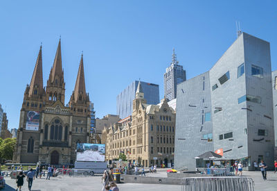 People walking in city against clear blue sky