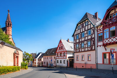 Road amidst buildings against clear blue sky